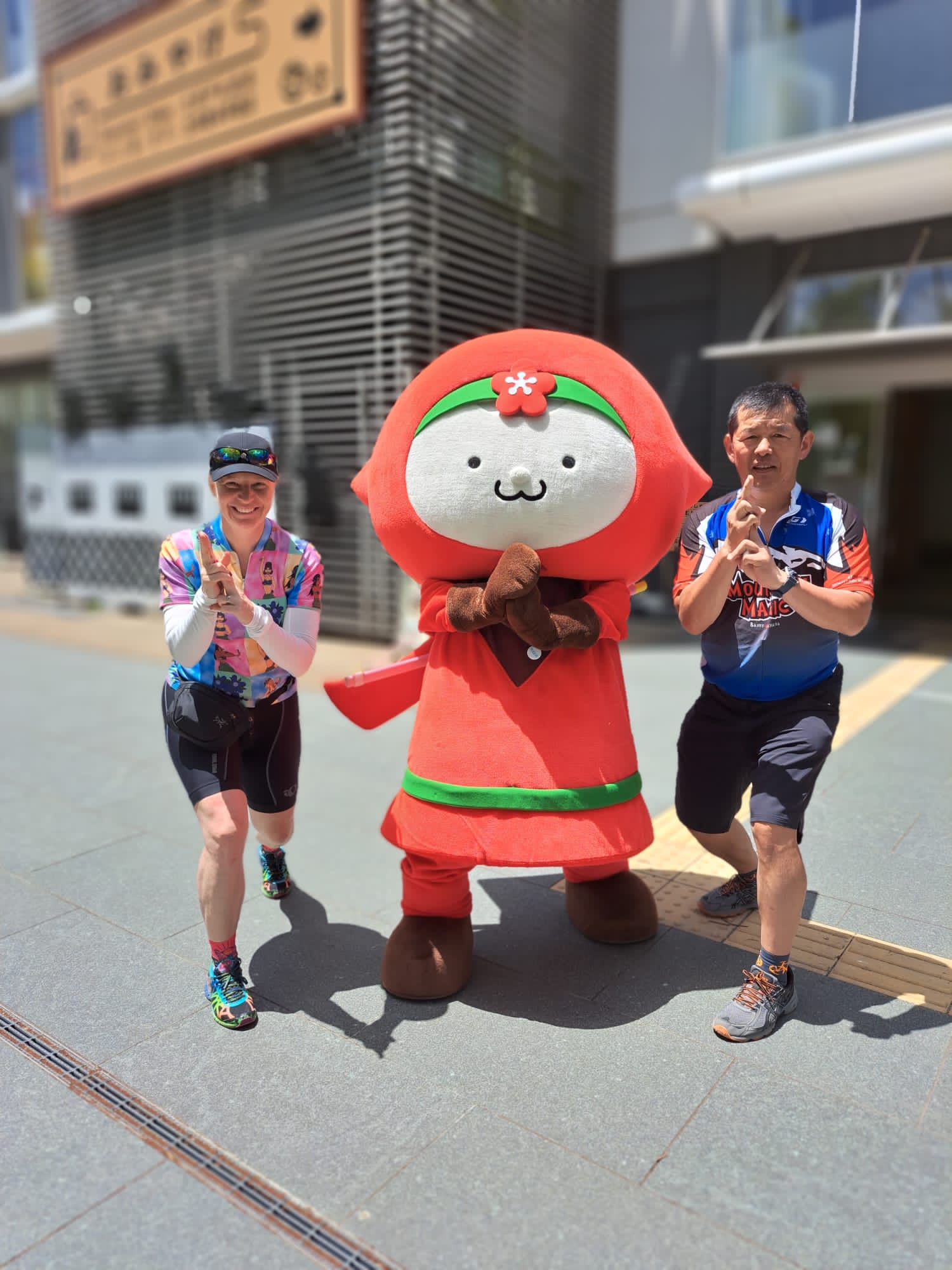 Two people in a ninja pose on either side of a red plum mascot at Wakayama castle.