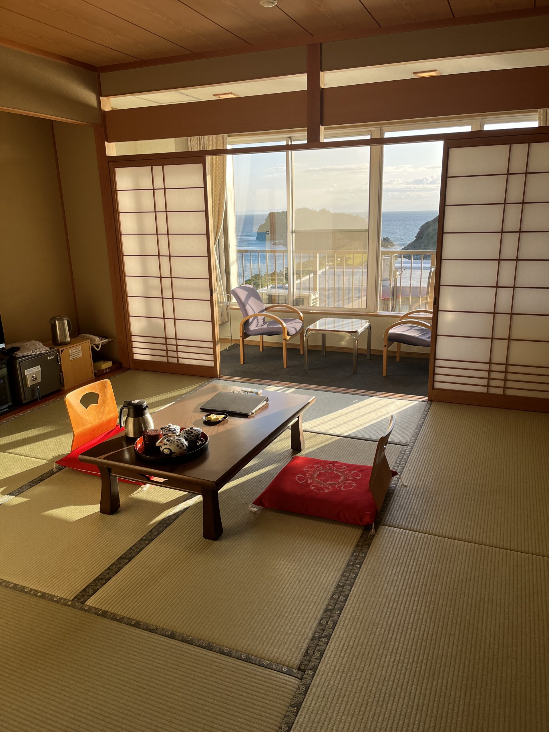 Japanese Ryokan hotel with tatami floors low table with two chairs, window with view of the ocean in the background.