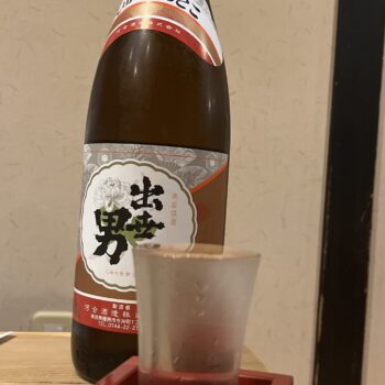 Bottle of large sake in background with a cup in a square dish serving the sake.