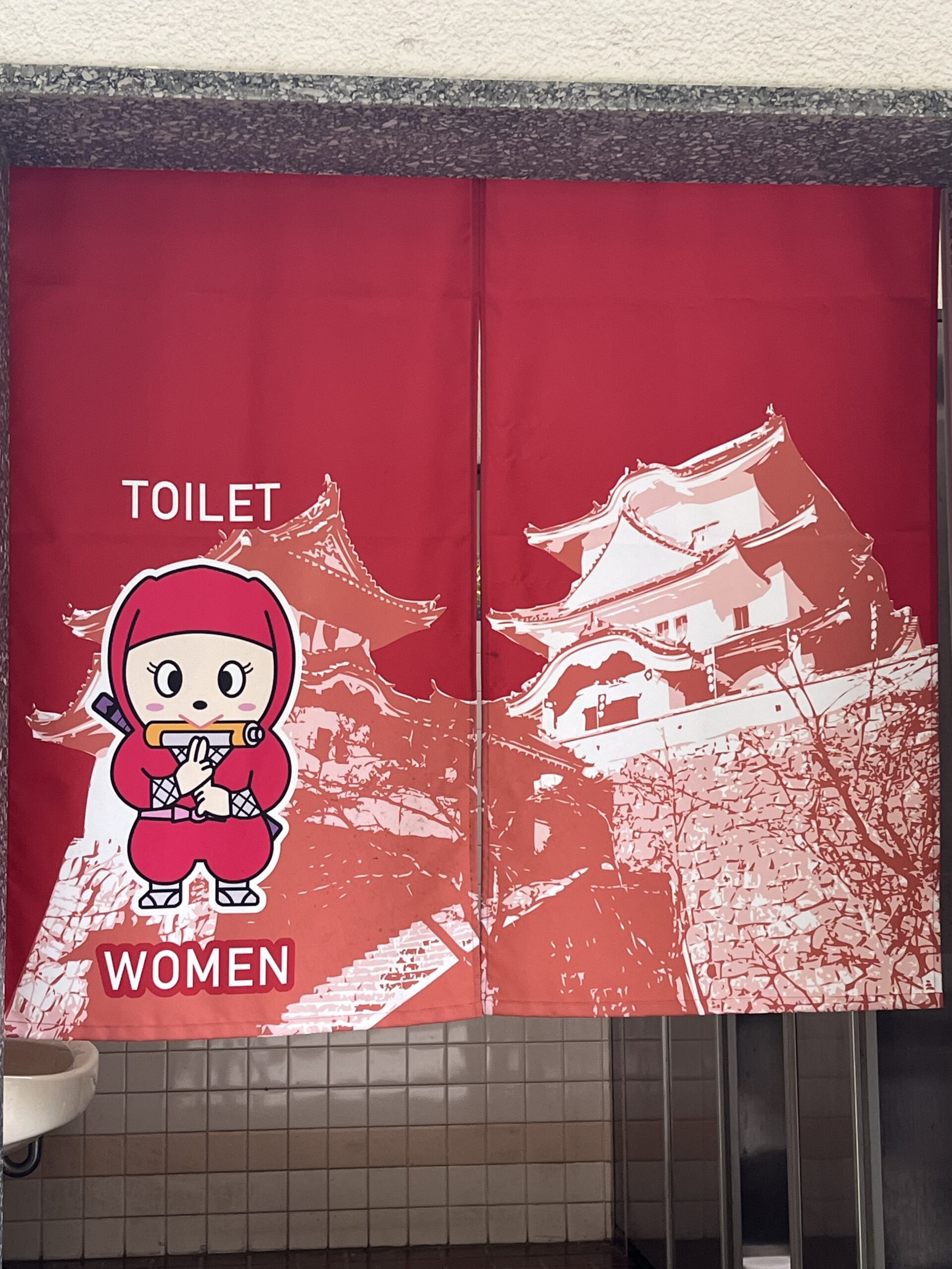 Red curtain with a picture of a female ninja and castle that marks the entrance of the woman's toilet. Iga-Ueno Japan.