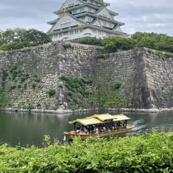 Osaka castle with golden cruise boat in river in front of the castle