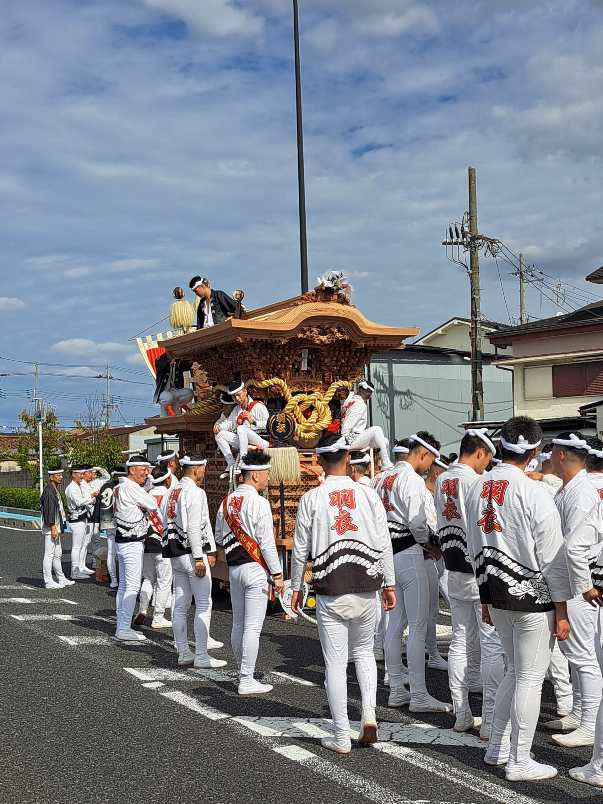 Men in white with black stripe jackets and white pants standing around a Danjiri wooden Japanese float getting ready to push it down the street for a local street festival - Omatsuri, in southern Osaka.