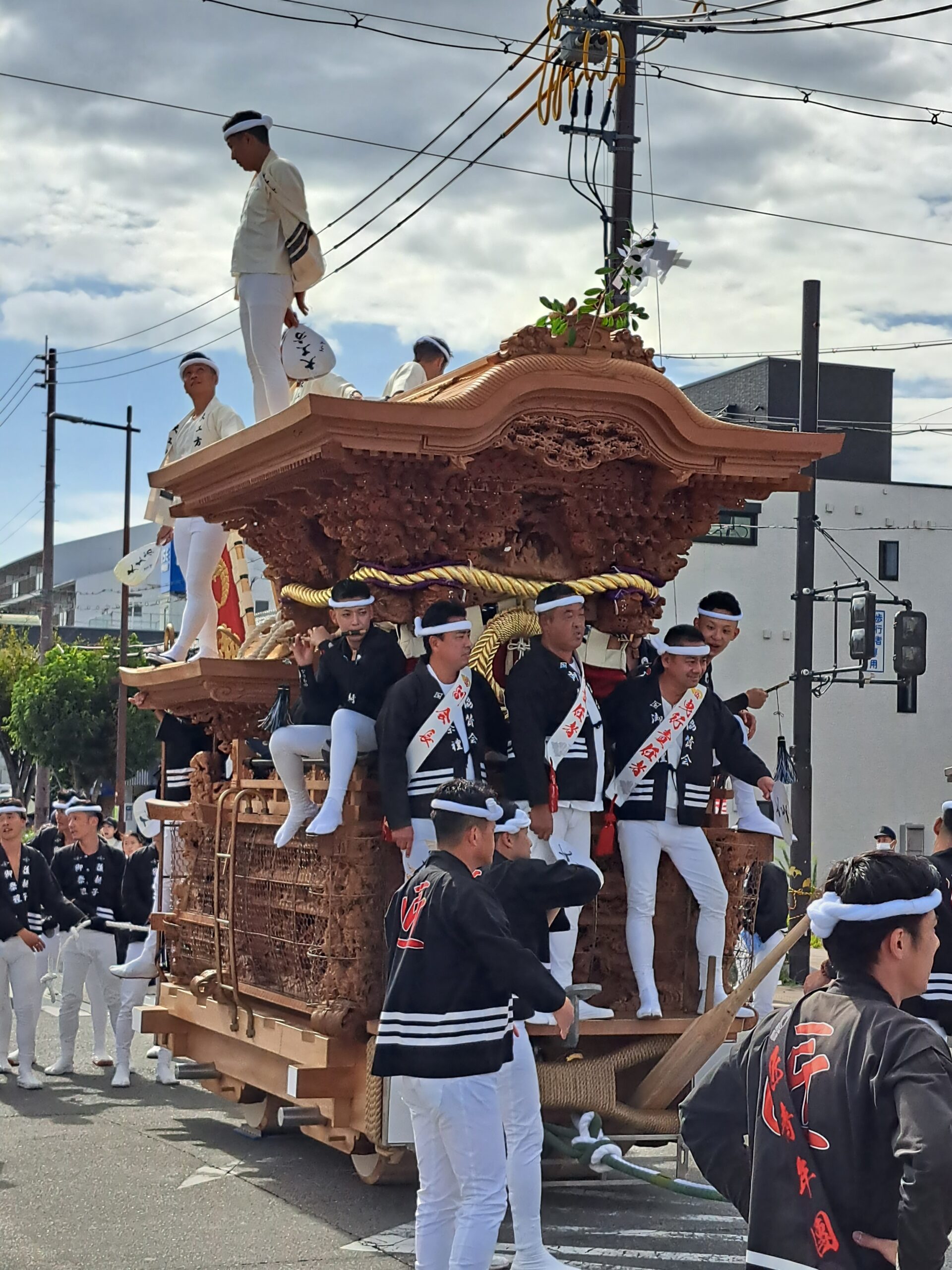 A Danjiri festival float begin moved in the street in south Osaka with men in dark jackets and white pants pushing the float and mean with flags and fans on the top chanting as the float goes along the street.