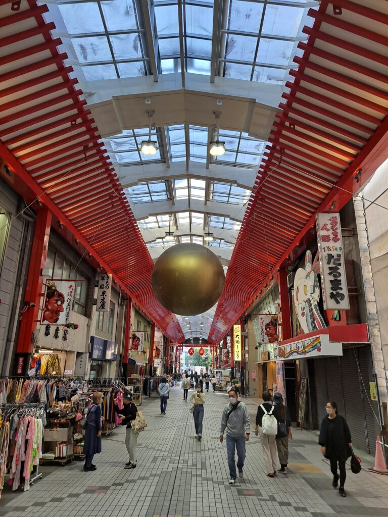 Japanese covered shopping street in Osaka with large golden ball hanging.