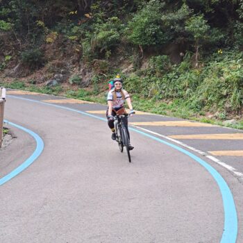 A smiling cyclist coming downhill on a paved road with blue bike lines on the path.