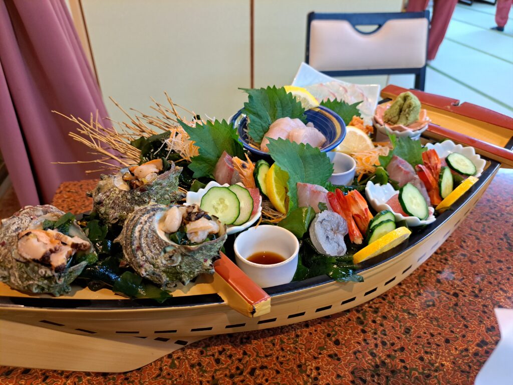 A small wooden boat serving fresh seafood including orange shrimp, seashells, tuna, lemon wedges, cucumbers.