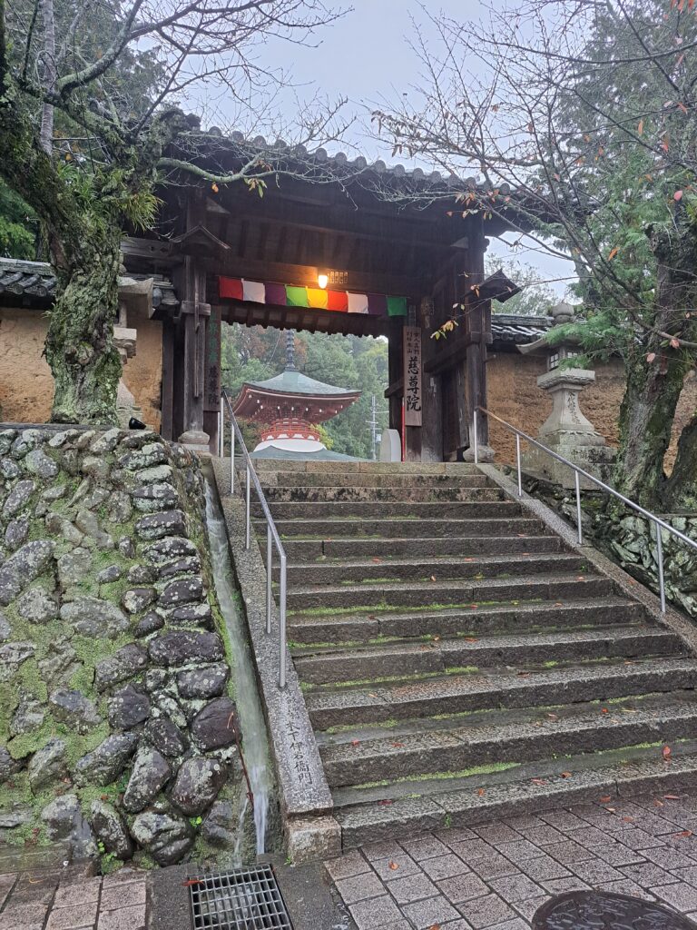 Small staircase going to a temple entrance. A top of a red temple is showing through the entrance. A multi-colored material hangs above the entrance.