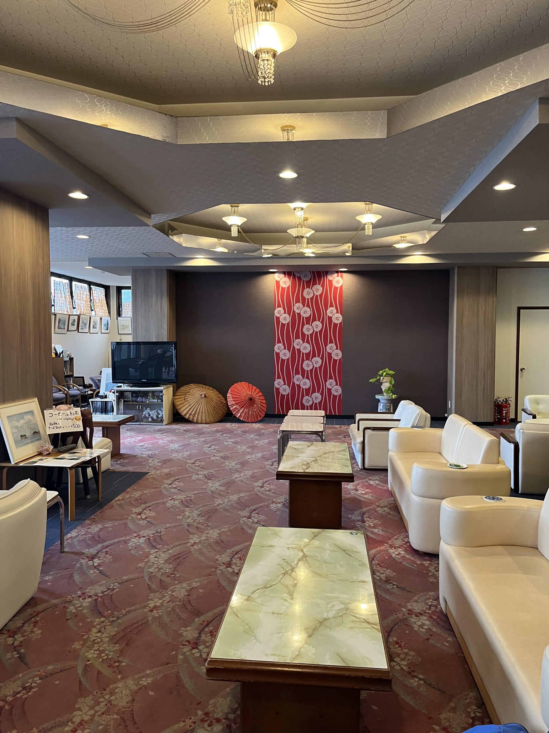 The lounge area at Ryokan Futagojimaso resort in Wakayama. The red flower pattern at the end of the room and white leather sofas with low marble tables.