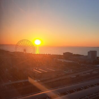 Sunset at Rinku town Osaka with the yellow sun setting on a slice of the ocean. A Ferris wheel is on the right side with miscellaneous buildings in the front of the picture.