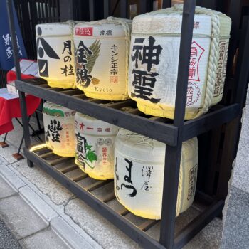 Sake barrels with three on top shelf and three on the bottom shelf in front of a restaurant in Kyoto.