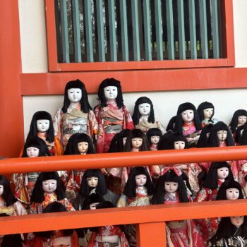 Awashimi Jinja. Also known as the doll shrine in Wakayama. Japanese dolls with white faces, dark long straight hair and mostly red kimonos are lined up behind the red wood of the temple.