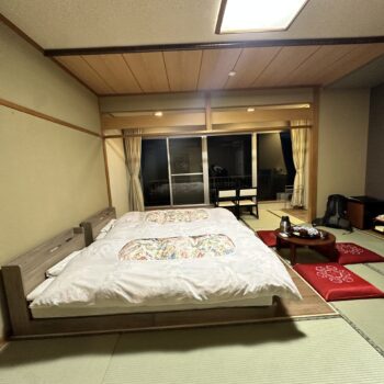 Japanese Roykan with western style bed frames, three red cushions around a low dark wooden table at the foot of the two beds. A large window is at the end of the room dark in the night.