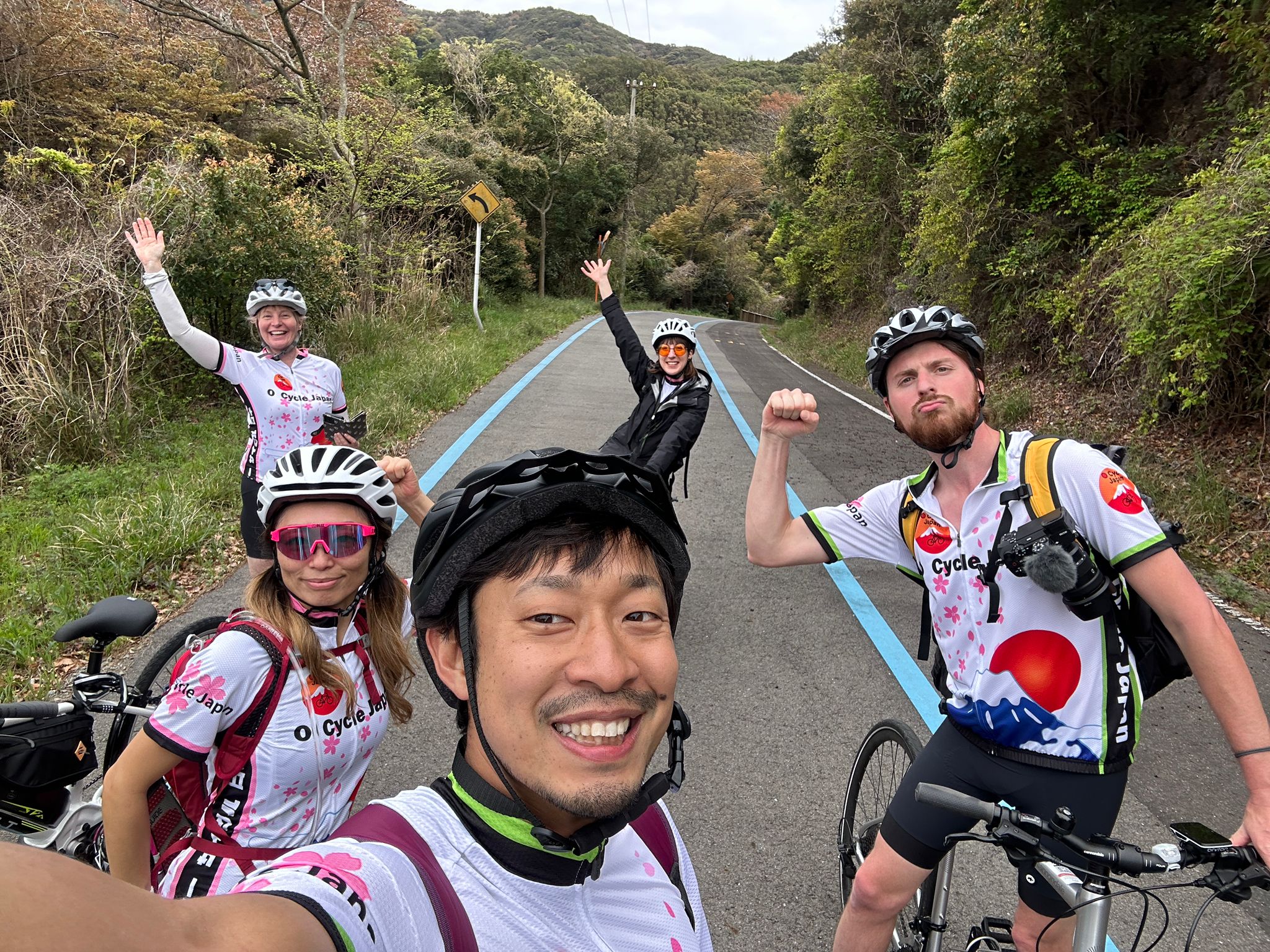 Five excited cyclists some with their hands or fists in the air to show their excitement after concurring a hill climb.