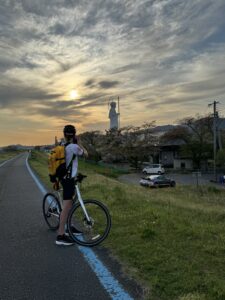 Cyclist stops and looks back at the sunsetting on the bike path, with a statue of a large Buddha in the background.
