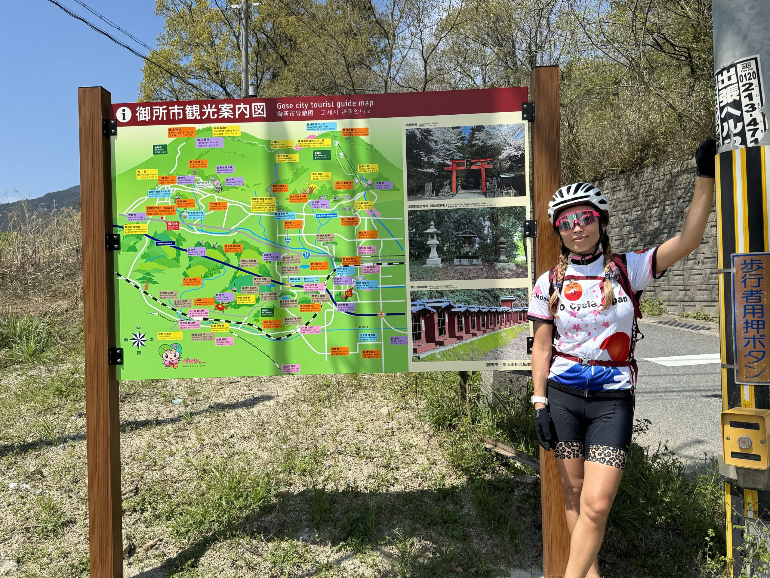Cyclist stands next to brightly colored map of local sightseeing spots in rural Japan.