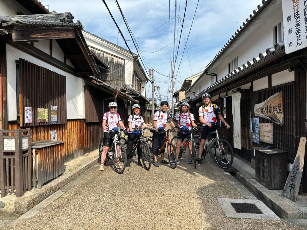 Group of cyclists pose with their bikes on an old traditional Japanese street.