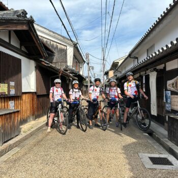 Group of cyclists pose with their bikes on an old traditional Japanese street.