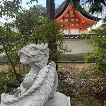 Dragon statue at a shrine with red and wood roof of shrine in rural Japanese in the background.