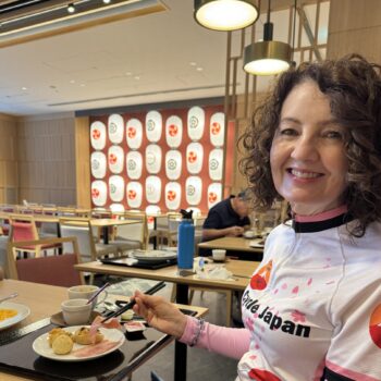 Woman smiles as she enjoys her breakfast. Paper lanterns in white, orange and grey are in the background.