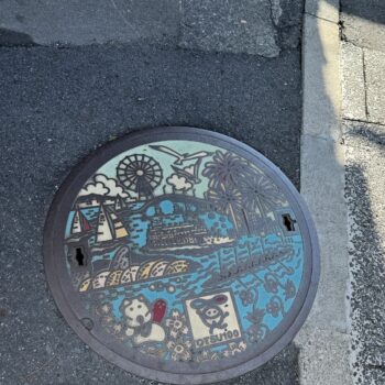 Manhole cover from Otsu Japan depicting a ferries wheel, the lake, sail boats, a ferry and the lake.