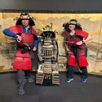 Two people dressed in red samurai costumes pose with gold Samurai suit in the middle.