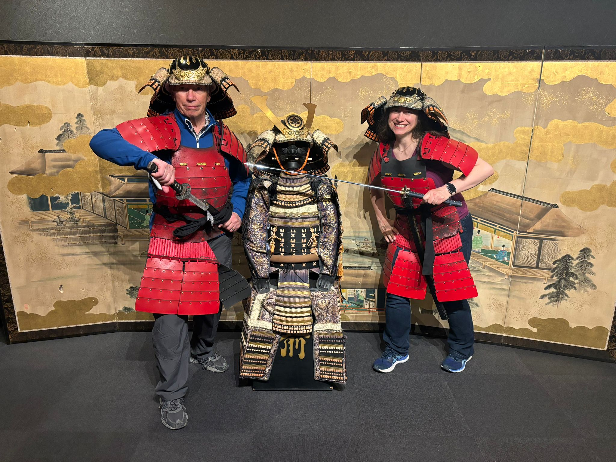 Two people dressed in red samurai costumes pose with gold Samurai suit in the middle.