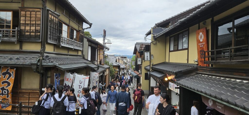 Kiyomizu- Zaka street view shows old Japanese buildings lining a street full of people in Kyoto.