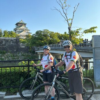 Osaka Castle in background with a bridge Two cyclists pose with their bikes in front.