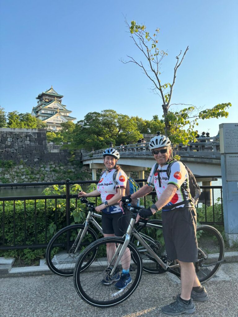 Osaka Castle in background with a bridge Two cyclists pose with their bikes in front.