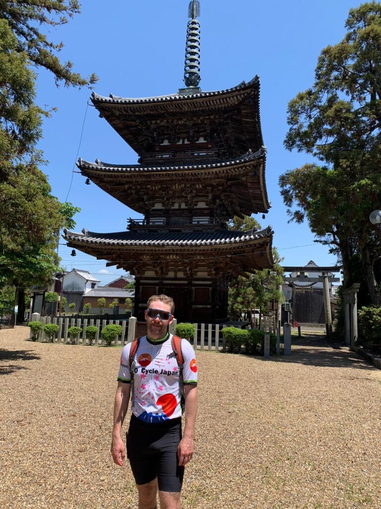 Cyclist by Pagoda. Cyclist with O Cycle Japan jersey stands in front of a three story pagoda.