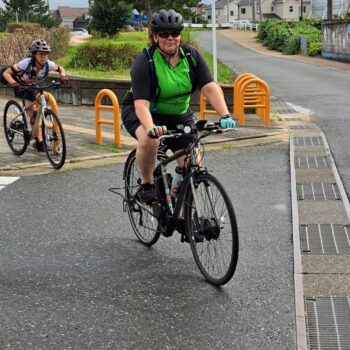 Woman in green and black jersey cyclists on a road.