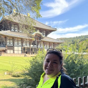 Person in yellow cycling jersey stand in front with a large old building in the background. This is Todaiji temple