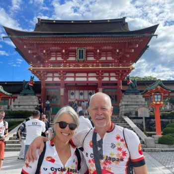 Couple poses in cycling shirts in front of red Buddhist gate.