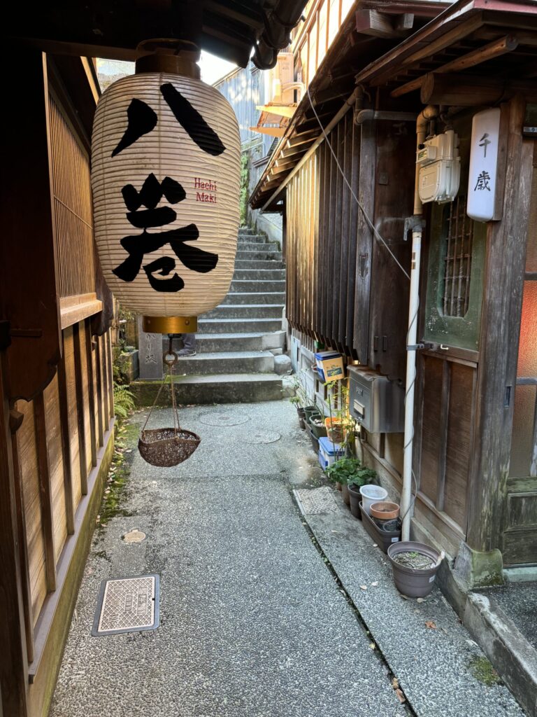 White paper lantern hangs from storefront on narrow street with stairs in background in a Chaya neighborhood in Kanazawa.