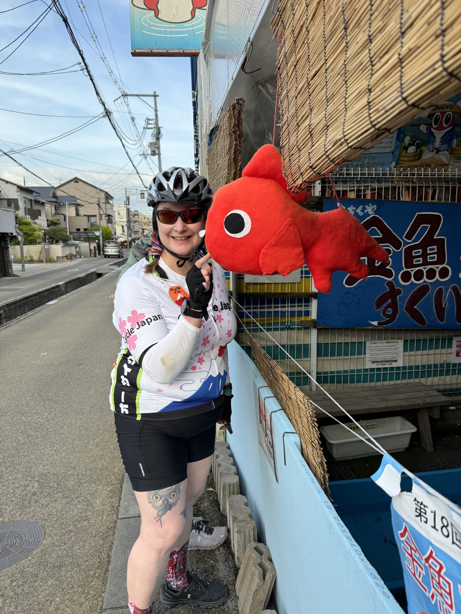 Cyclist gets close to red stuffed fish hanging from a storefront.