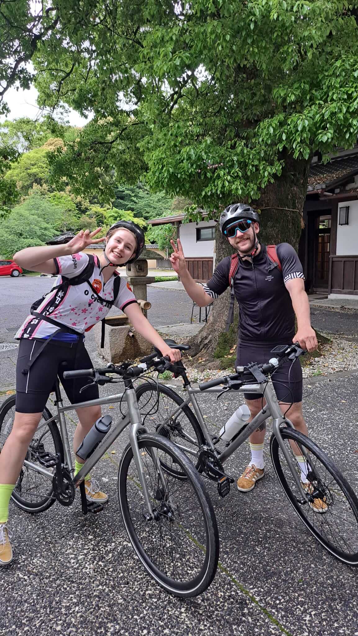 Two happy cyclists pose with their bikes while giving the peace sign in Japan.