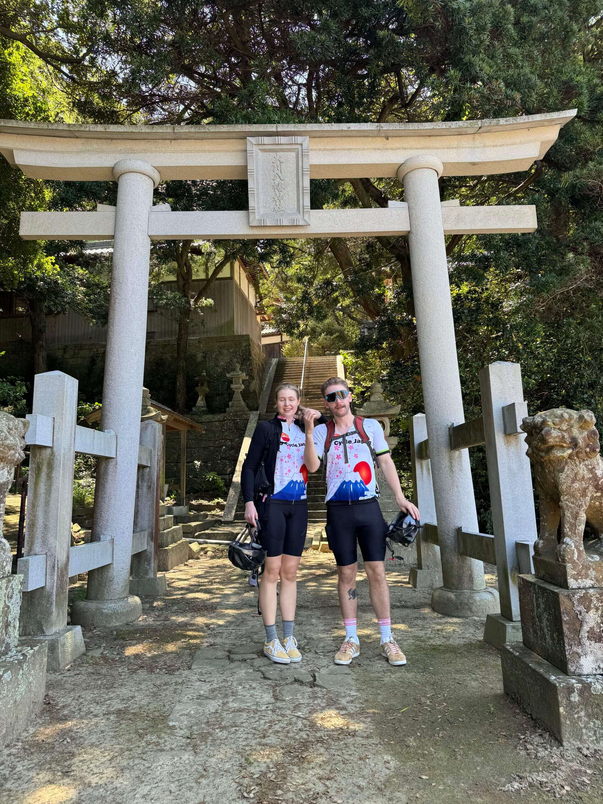 Two cyclists pose in front of a Tori Gate - entrance to a Shinto shrine
