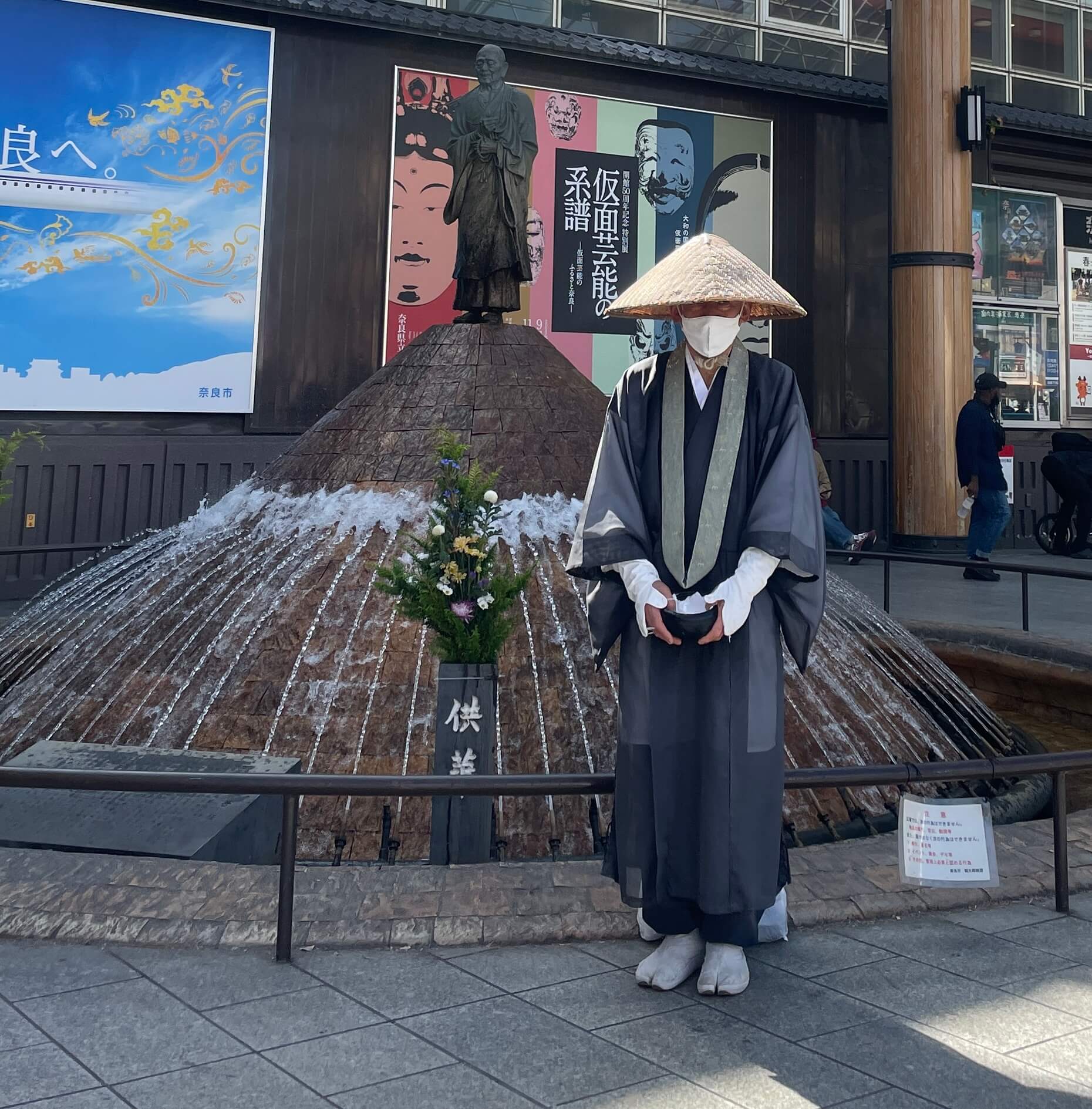 Buddhist monk stands outside statue in Nara collecting donations.