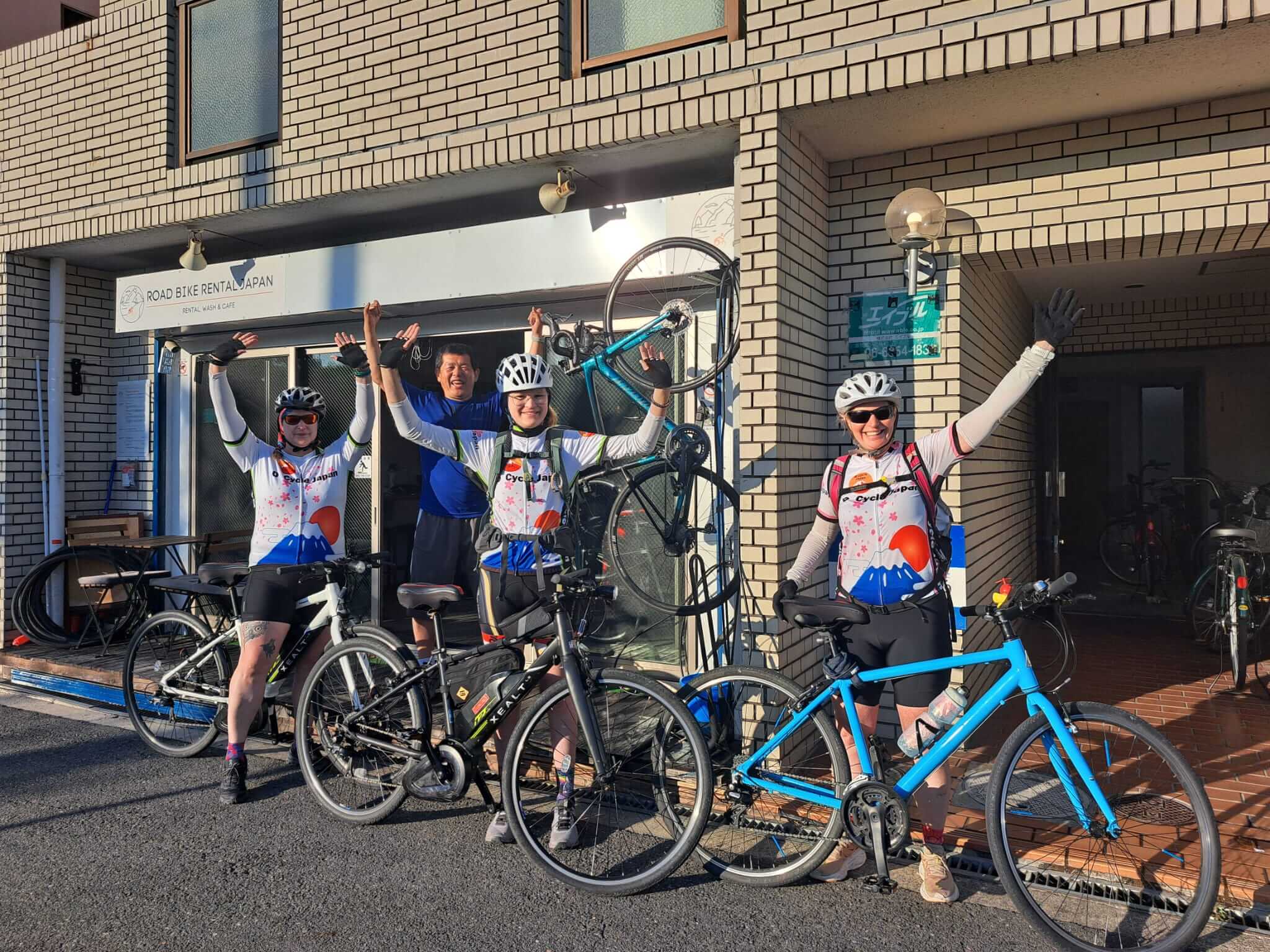 Three cyclists celebrate outside Road Bike Rental Japan after successfully completing a cycle tour in Japan. Amazing adventure seekers.