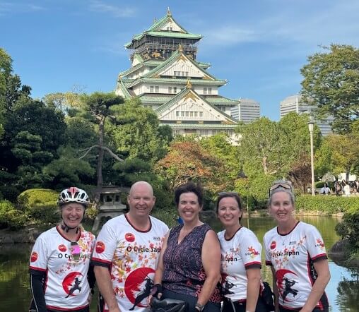 Group of cyclists post in front of Osaka Castle in their O Cycle Japan cycle jersey's and smiles.