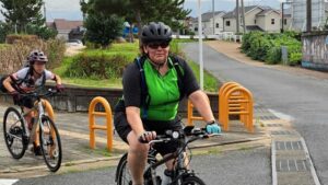Woman in green and black jersey cyclists on a road.