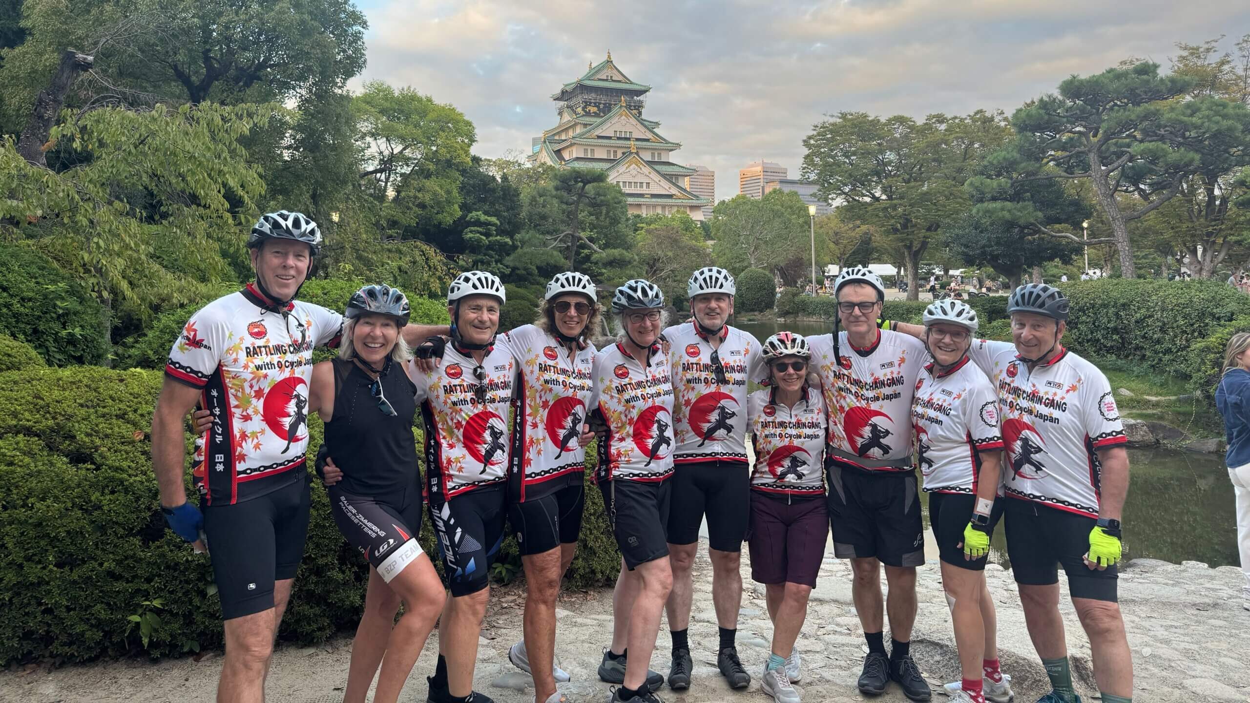 A group of 10 cyclists pose with Osaka castle in the background. Most wear a O Cycle Japan jersey.