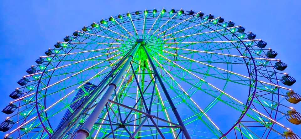 Ferris wheel in Rinku Town, near the Kansai International Airport in Osaka, Japan. Bright blue sky with bright green Ferris Wheel. In the background you can see the tall Rinku Gate Tower.