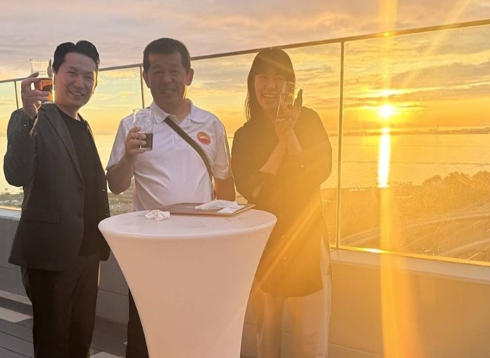 Rinku town sunset Rinku town sunset from Yona Yona moon walk roof top beer bar. Three people smile with the bright sun setting behind them.