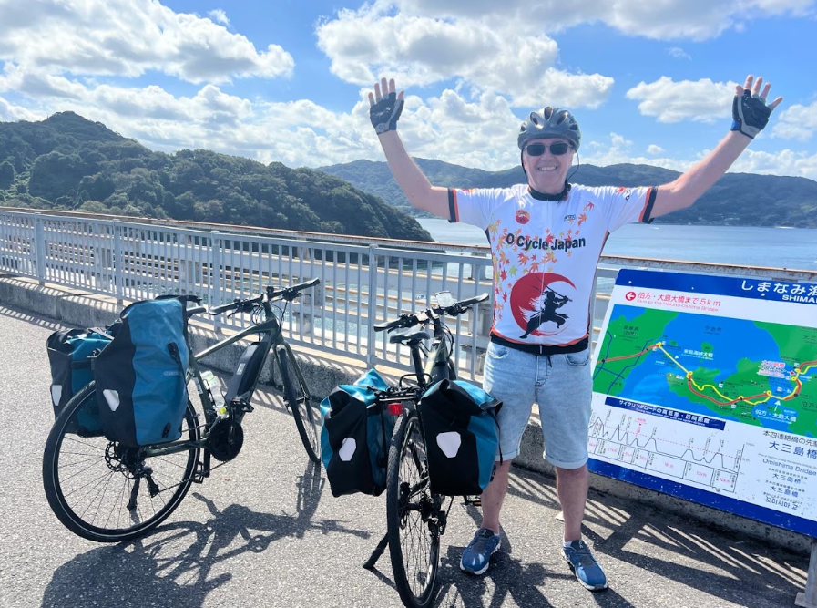 Cyclist has hands in the there with map and ocean in the background as they cycle the famous Shimanami Kaido route.